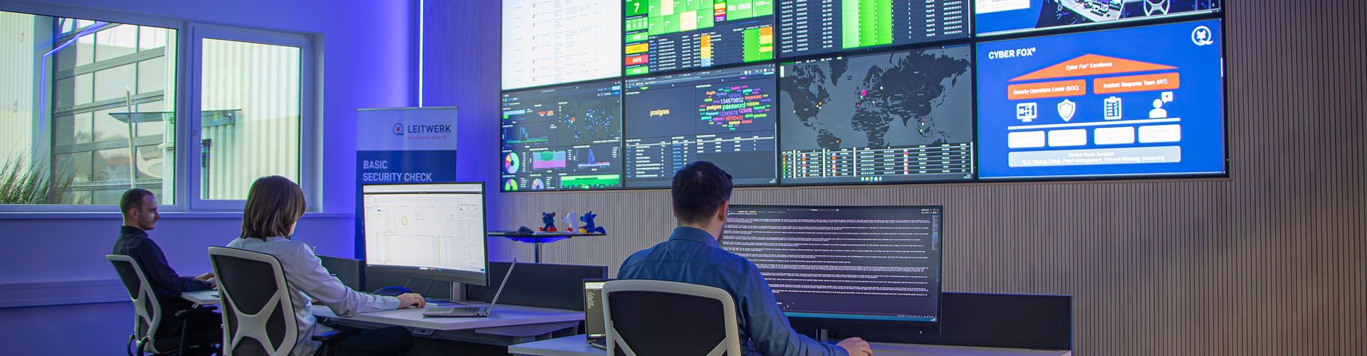 3 Mitarbeitende sitzen im Security Operations Center und überwachen Monitore